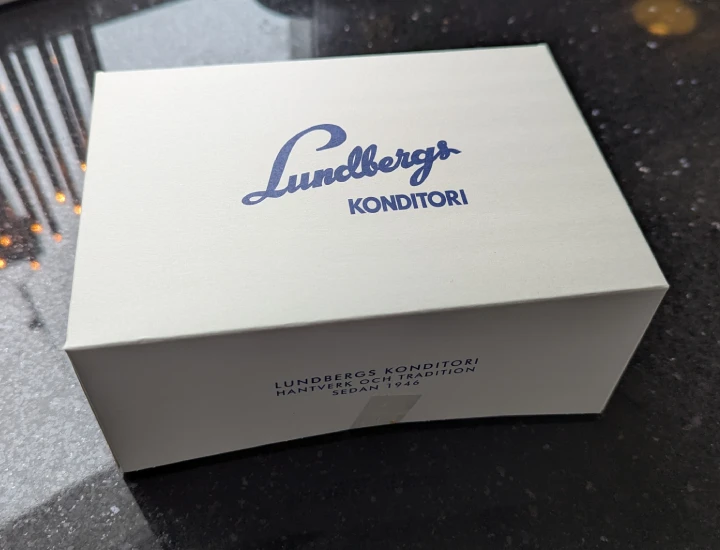 A Lundbergs pastry box. It's a rectangular white cardboard box with blue print. On the lid Lundbergs Konditori is printed in the same style as the neon sign on the roof of the store. On the front the text says Lundbergs konditori and (translated from Swedish) craft and tradition since 1946.