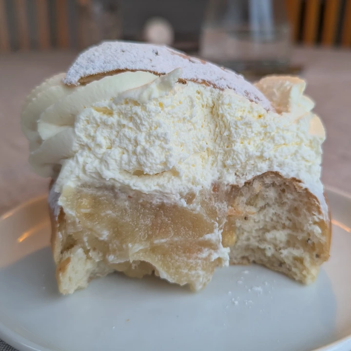 A view of the inside of a semla. The almond paste filling is lightly coloured. Some slithers of almond can be seen mixed amongst it. The cream is plentiful and is about half of the height of the bun.